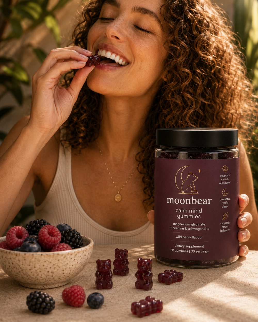 Woman enjoying a moonbear wild berry gummy in warm natural light, jar in hand beside a bowl of berries